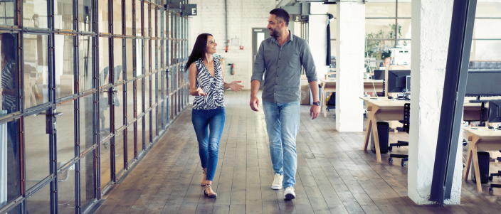 Coworkers chat happily while they walk through an office setting.