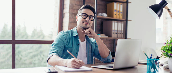 Man sitting at desk with computer while thinking with pencil and paper.