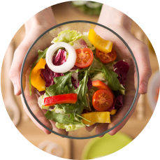 Hands holding a bowl of fresh salad, filled with onion slices, tomatoes, lettuce, and colorful peppers.