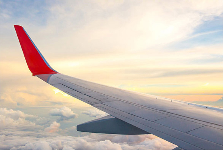 The wing of a Delta airplane flying above the clouds in a blue sky.