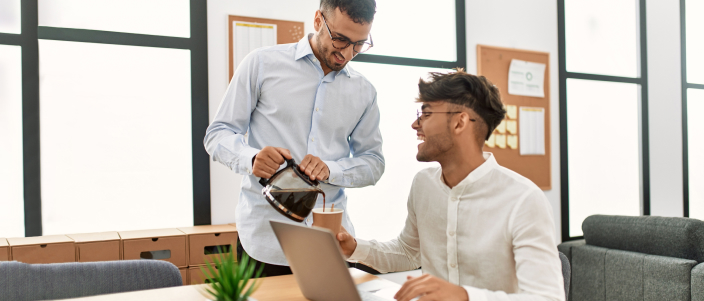 Man kindly pours coffee for a coworker at a modern office.